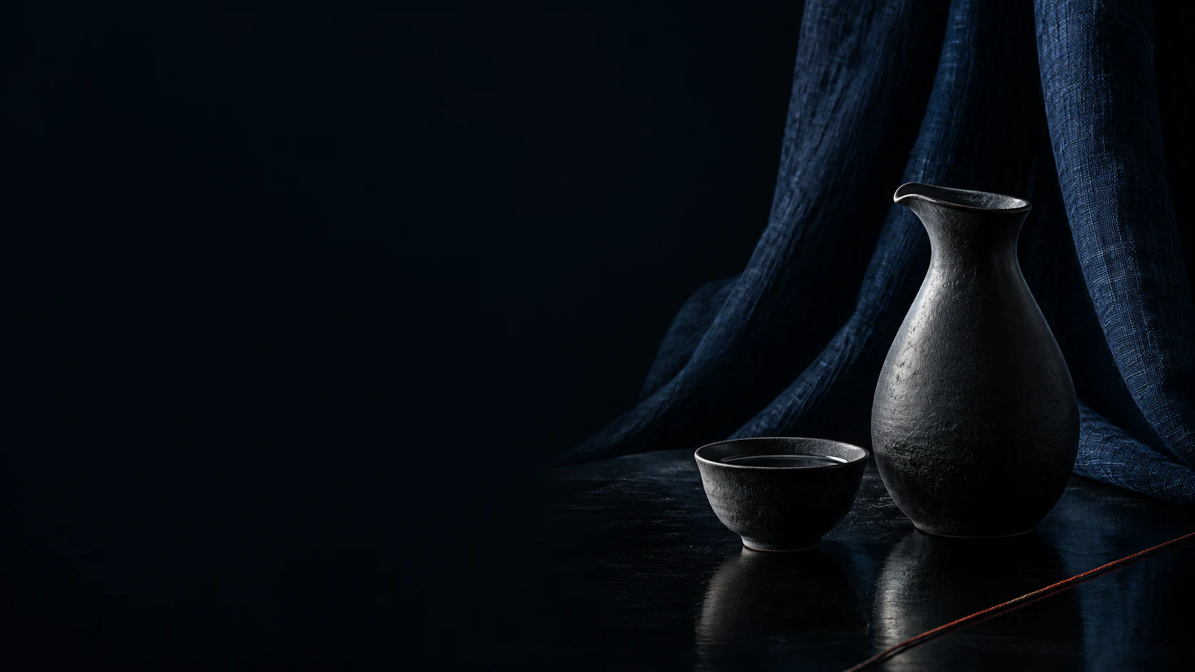 Black sake vessels set against layered indigo, joined by a restrained red IKI thread.